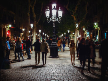 Barcelona Street Photography, curlicue street lamp, narrow tree alley, pedestriants passing, romantic night walk