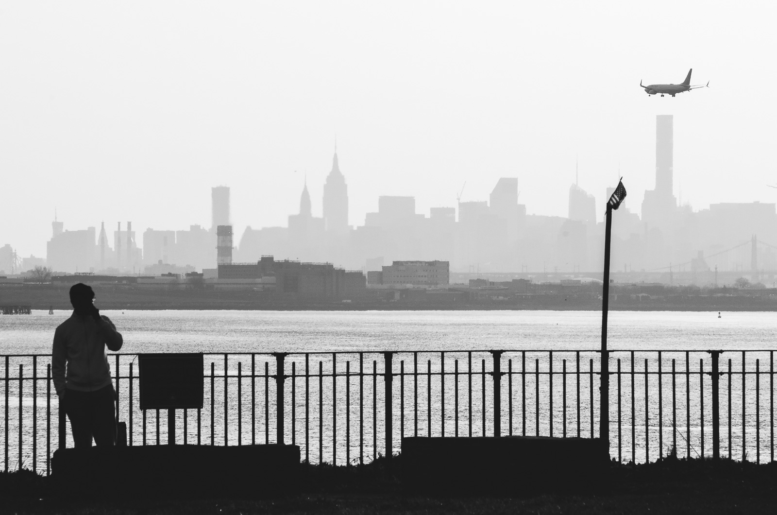 A man watches an Airplane flying over the distant Skyline of Manhattan to land on the LaGuardia Airport.
