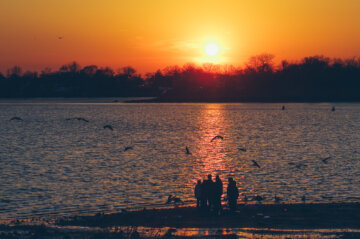 A family watches the Sunset while standing on the shore of the Ferry Point Park in the Bronx, New York City