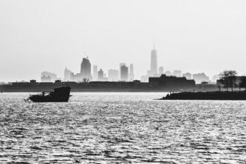 A Ship Wreck is lying in the East River with the distant Skyline of Manhattan in the Background