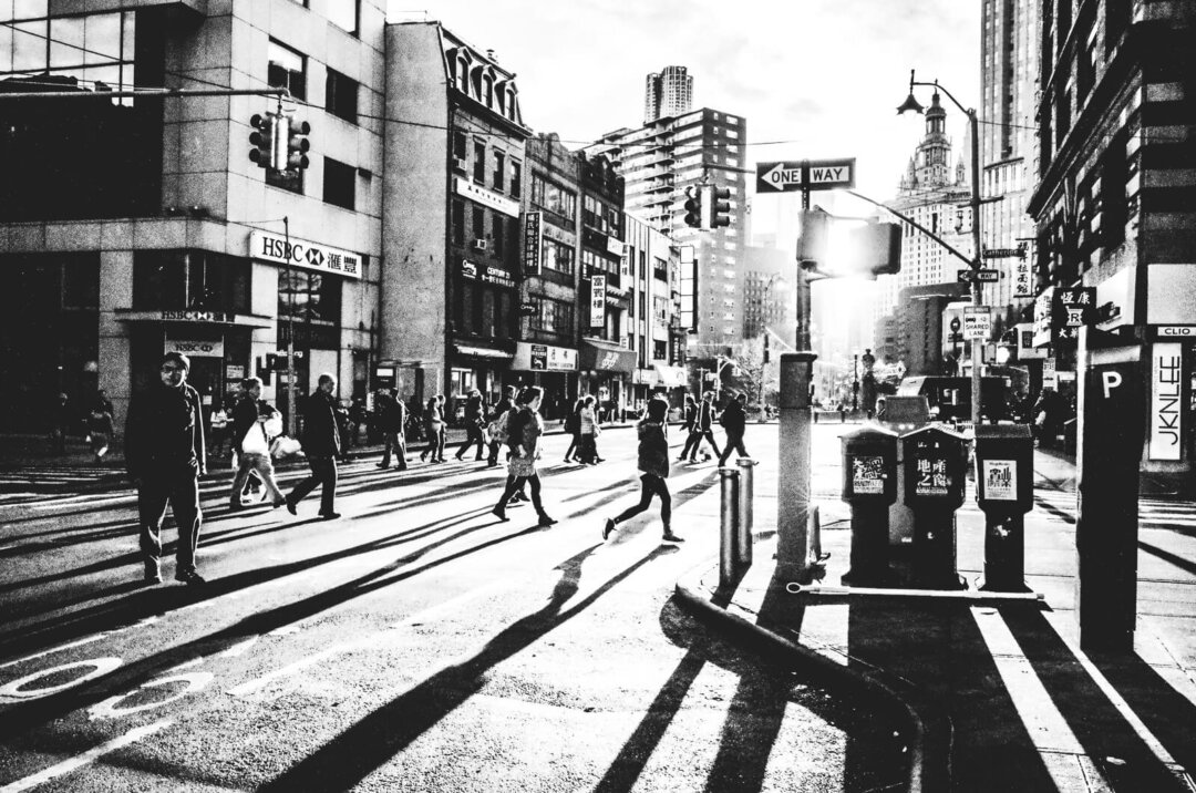 People walk and cast long silhouette shadows on East Broadway Street during Sunset in New York City