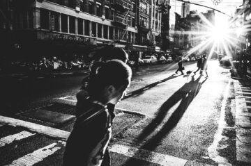 People cast long shadows along East Broadway Street in New York City