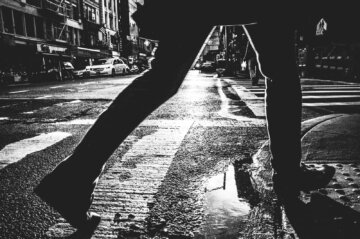 Man steps over a  puddle onto a sidewalk on East Broadway Street in New York City